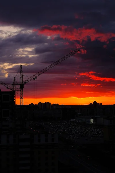 Tower crane, new buildings, Parking and cars in the distance during the sunset of the city, against the sky. Beautiful night city. Residential area with houses under construction.