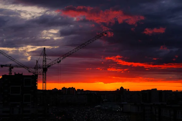 Tower crane, new buildings, Parking and cars in the distance during the sunset of the city, against the sky. Beautiful night city. Residential area with houses under construction.