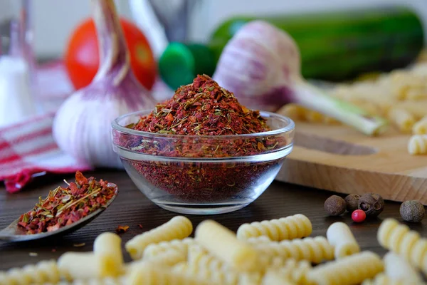 Dry Georgian spices or spicy adjika for gourmets, in a glass Cup. Next to garlic, red tomatoes, olive oil, pasta on a wooden table. The concept of organic farm products. Vegetarian and vegan food.