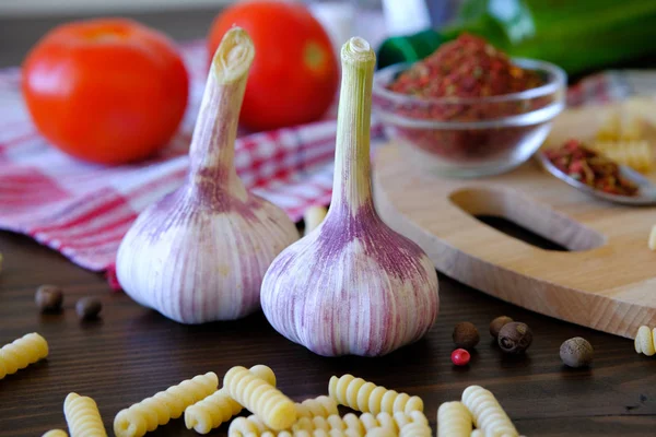 Garlic, red tomatoes, dry Georgian spices for gourmets, olive oil, pasta on a wooden table. The concept of cooking, natural organic farm products. Vegetarian and vegan food. Selective focus.