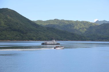 Bir tekne gölde seyahat ediyor. Tekne beyaz ve üzerinde birkaç kişi var.