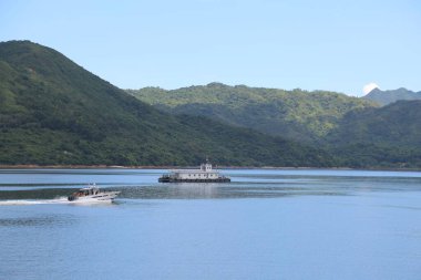 Bir tekne gölde seyahat ediyor. Tekne beyaz ve üzerinde birkaç kişi var.