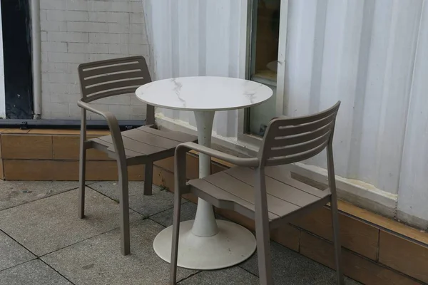 Beyaz plastik bir masa, iki sandalye, gri plastik bir sandalye ve bir binanın yan tarafında mermer bir yuvarlak masa. minimalist, ürün fotoğrafçılığı.