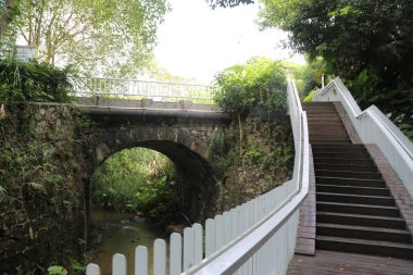 Beyaz kazıklı çit, taştan köprünün yanında, akan suyun üzerinde ve yukarı doğru yükseltilmiş tahta bir merdiven var. Merdivenler kemerin bir tarafından diğer tarafına gidiyor..