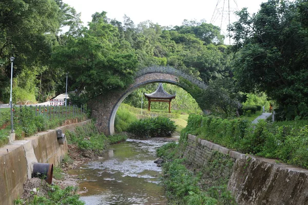 Nehrin üzerindeki taş kemer köprüsü Shenzhen Nanshan Parkı 'nda her iki tarafında yeşil ağaçlar ve çayırlarla çevrili ve yanında eski moda bir Çin evi bulunuyor..