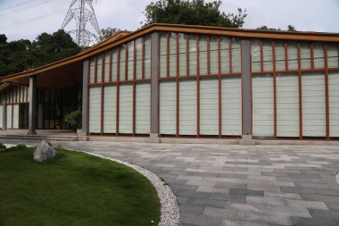 Geniş cam pencereli, ahşap çerçeveli, yeşil çimenler ve beton zeminle çevrili modern bir Çin tarzı müze binası. Yapının dış duvarlarında açık gri ahşap aksanlar var.