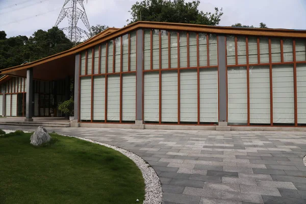 Geniş cam pencereli, ahşap çerçeveli, yeşil çimenler ve beton zeminle çevrili modern bir Çin tarzı müze binası. Yapının dış duvarlarında açık gri ahşap aksanlar var.