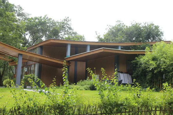 Ormanda, ahşap elementler, yeşil çimenler ve etrafındaki ağaçtan yapılmış bitkilerle modernist bir ev. Binanın doğaya bakan geniş pencereleri var. Ağaçlar ve uzun çalılarla çevrili..