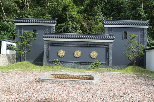 Önünde üç adet yuvarlak altın oyması olan gri bir duvar. Açık hava mezarlığında çakıl ve çimlerle çevrili. Toprak, sessiz tefekküre yardımcı olması için her mezarın etrafında açık renkli çakıl taşlarıyla kaplıdır.