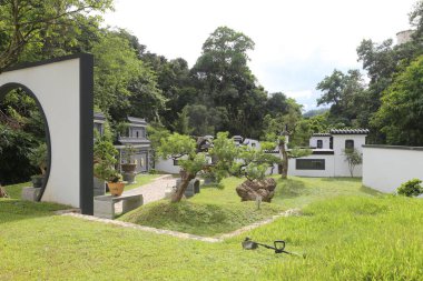 Parkta, yeni Çin tarzı basit mimarinin her iki tarafında beyaz duvarlar ve yeşil ağaçların olduğu açık bir alan var, modern bir manzara bahçesi yaratıyor..