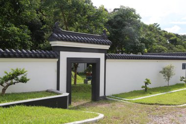 Çin tarzı bahçe kapısının beyaz duvarlarının üzerinde yeşil çimenler ve ağaçlarla çevrili siyah fayanslar vardır. Giriş açık ve kenarındaki araçları park etmek için bir alan var..