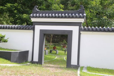 Üzerinde siyah kiremitler olan beyaz bir duvar, girişinde çimenlere ve ağaçlara açılan kemerli bir kapı var. Kapının çatısında Çin tarzı bir mimari var ve çitin içinde çiçek ve bitki yetiştirmek için küçük bir kare kap var.