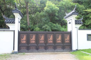 Arka planda yeşil ağaçlarla çevrili, beyaz duvarları ve siyah ahşap oymaları olan basit bir Çin tarzı çift kapılı kapı. Ana gövde, üzerine geleneksel dekoratif desenler oyulmuş bakır plakadan yapılmıştır.