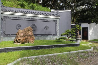 Çin usulü bahçe, iki duvarın solunda Çin ejderhası desenli gri duvar ve önünde düz bir zemin, alt kenarında yeşil çimen..