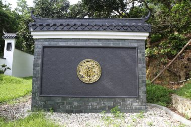 Üzerinde altın ve siyah amblem olan taş bir duvar. Duvar tuğladan yapılmıştır. Duvarın önünde yeşil bir çim alanı var.