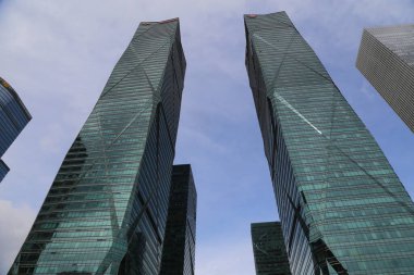 Şenzen şehrindeki modern gökdelenler, Çin 'de, cam perde duvarları var. Mavi gökyüzüne karşı yan yana duran iki yüksek bina alçak bir açıdan görülüyor.