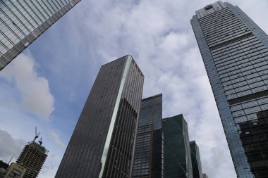 Finans bölgesindeki yüksek binaların alçak açılı fotoğrafı, cam cepheli gökdelenlere bakıyor. Şehrin gökyüzü bulutlu bir gökyüzüne karşı görünür..