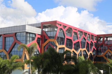 a building in the shape of hexagons with red and pink walls, set against a tropical landscape in daylight. the architecture features an office complex with a front view