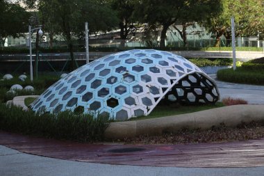 A large dome shaped structure is in a park. The dome is made of metal and has a glass roof. The structure is surrounded by plants and grass
