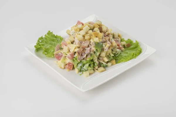 Beyaz arka plan üzerinde izole beyaz tabakta taze yeşillikleri ile dekore edilmiş mayonezli Olivier Rus salatası