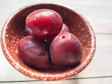 Olgun kırmızı erik ahşap bir masa üzerinde kahverengi bir seramik kase.