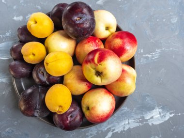 Olgun nektarin ve yuvarlak bir gri Seramik plaka, üstten görünüm üzerinde kırmızı erik. Gri arka plan beton için