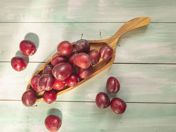 Red plums in a decorative wooden platter on a wooden background closeup