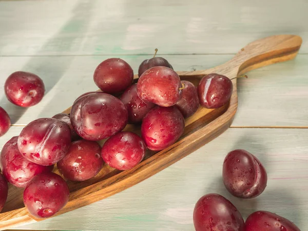 Red plums in a decorative wooden platter on a wooden background closeup