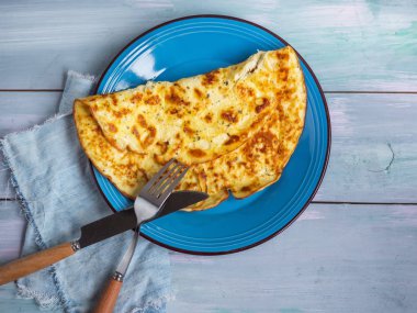 Hafif bir kahvaltı ile mavi seramik plaka üzerinde süzme peynir omlet ve mavi bir arka plan ile bir ahşap tahta.