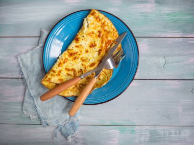 Hafif bir kahvaltı ile mavi seramik plaka üzerinde süzme peynir omlet ve mavi bir arka plan ile bir ahşap tahta.