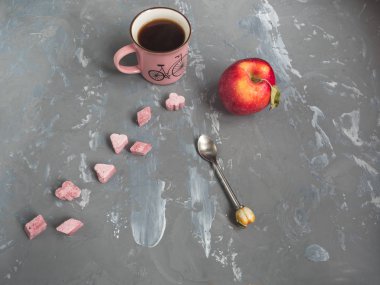 Kırmızı elma, bir fincan kahve ve pembe Lump & şeker, gri bir arka plan üzerine bir çay kaşığı