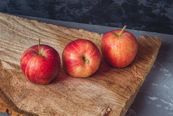 Three ripe red apples lie on a wooden saw cut close up