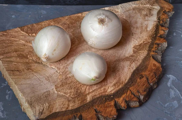 Three white onions on a wooden saw cut close up, gray background