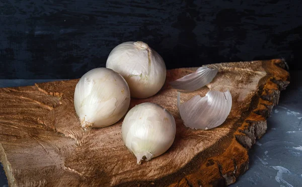 Three white onions on a wooden saw cut close up, gray background