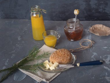 Kahvaltı susam çörek, portakal suyu ve reçel oluşur. Tereyağı, çatal bıçak takımı.