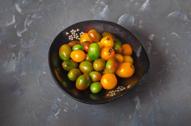 Yukarıdan küçük sarı ve yeşil domates siyah bir tabak içinde görüntülemek