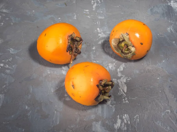 Três Persimmons Amarelos São Triângulo Uma Tabela Cinzenta — Fotografia de Stock