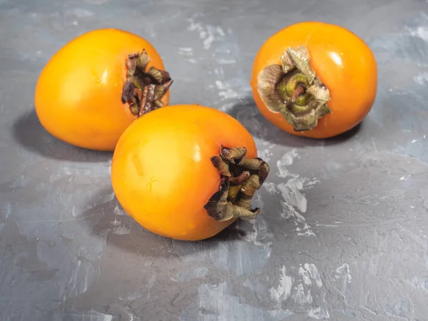 Três Persimmons Amarelos São Triângulo Uma Tabela Cinzenta Vista Lateral — Fotografia de Stock