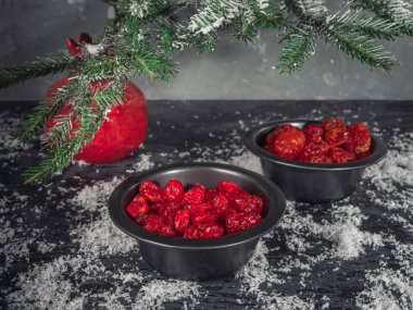 Set kırmızı kurutulmuş meyveler siyah vazo içinde bir köknar dalı karanlık bir arka plan üzerinde kırmızı bir vazo. Bir saçılma kar. Noel kartı. kızılcık, kiraz