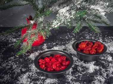 Set kırmızı kurutulmuş meyveler siyah vazo içinde bir köknar dalı karanlık bir arka plan üzerinde kırmızı bir vazo. Bir saçılma kar. Noel kartı. kızılcık, kiraz