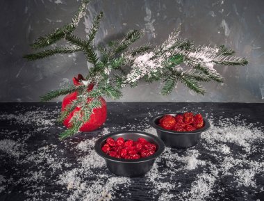 Set kırmızı kurutulmuş meyveler siyah vazo içinde bir köknar dalı karanlık bir arka plan üzerinde kırmızı bir vazo. Bir saçılma kar. Noel kartı. kızılcık, kiraz