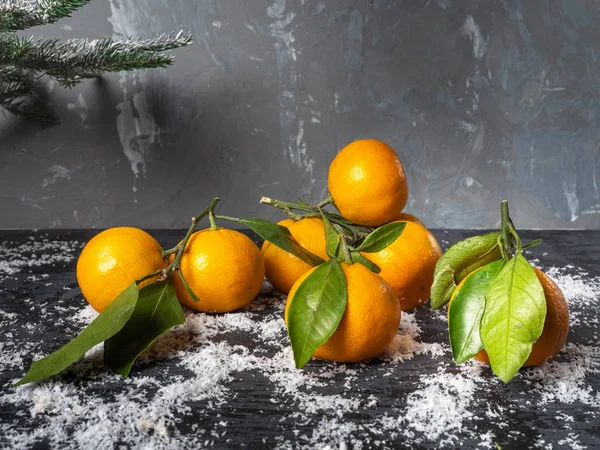 Mandalina kar bir saçılma karanlık bir zemin üzerine yeşil yaprakları ile. Şube üst köşesinde Ladin. Noel ruh hali.