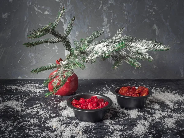 Set kırmızı kurutulmuş meyveler siyah vazo içinde bir köknar dalı karanlık bir arka plan üzerinde kırmızı bir vazo. Bir saçılma kar. Noel kartı. kızılcık, kiraz