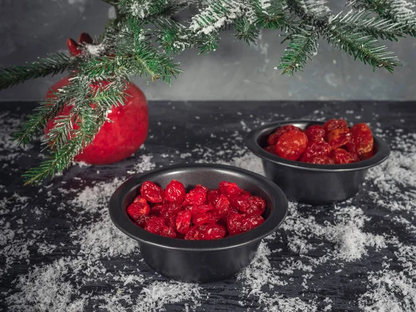 Set kırmızı kurutulmuş meyveler siyah vazo içinde bir köknar dalı karanlık bir arka plan üzerinde kırmızı bir vazo. Bir saçılma kar. Noel kartı. kızılcık, kiraz