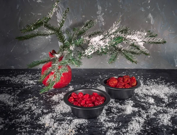Set kırmızı kurutulmuş meyveler siyah vazo içinde bir köknar dalı karanlık bir arka plan üzerinde kırmızı bir vazo. Bir saçılma kar. Noel kartı. kızılcık, kiraz