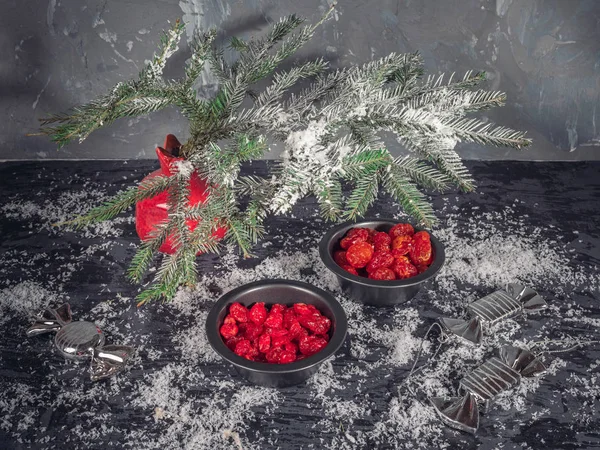 Set kırmızı kurutulmuş meyveler siyah vazo içinde bir köknar dalı karanlık bir arka plan üzerinde kırmızı bir vazo. Bir saçılma kar. Noel kartı. kızılcık, kiraz