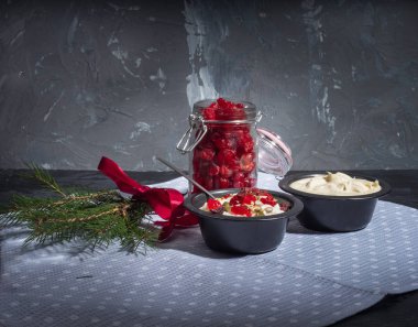 Hafif kahvaltı süzme peynir, ekşi krema, siyah vazolar, bir cam kavanoz ve arka planda bir plaser kurutulmuş kiraz süt süt ürünleri. Koyu arka plan. Çay kaşığı. Kırmızı kurdele ile Ladin Şubesi.