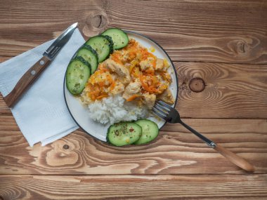 Tavuk ve pirinç keten peçete, taze salatalık dilimleri, çatal bıçak takımı ahşap bir masa üzerinde bir tabak içinde kahvaltı