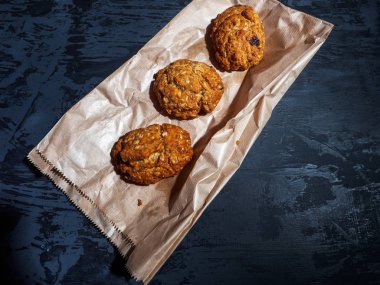 Üç yulaf ezmesi kuru üzüm kurabiyeleri, çapraz bir kağıt torba gri bir arka plan üzerinde bulunan. Yakın çekim.