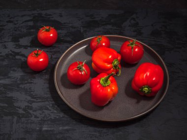 Kırmızı biber ve domates bir gri seramik tabak, yakın çekim, koyu arka plan üzerinde sebze kümesi